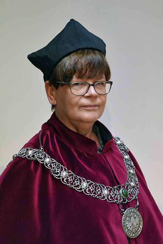 Zdjęcie Dziekan Wydziału Humanistycznego UZ dr hab. Małgorzata Łuczyk, prof. UZ W stroju reprezentacyjnym, występuje burgund płaszczu (todze) oraz ozdobnym łańcuchem z symbolami Uniwersytetu Zielonogórskiego.